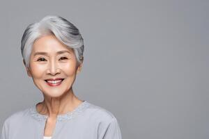 AI generated A portrait of an Asian lady, a smiling elderly woman with gray hair, stands on a gray background. A place for text, a banner for advertising. photo