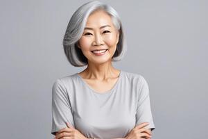 AI generated A portrait of an Asian lady, a smiling elderly woman with gray hair, stands on a gray background. A place for text, a banner for advertising. photo