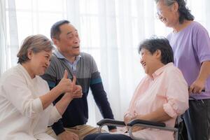 Asian young nurse support couple senior older woman in a wheelchair. elderly mature and a group of senior friends living in the hospital. socializing of retired people. photo