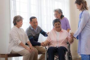 Asian young nurse support couple senior older woman in a wheelchair. elderly mature and a group of senior friends living in the hospital. socializing of retired people. photo