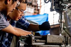 Asian worker in production plant drilling at machine. Professional worker near drilling machine on factory. finishing metal working internal steel surface on lathe grinder machine with flying sparks. photo