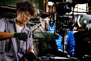 Engineer worker in production plant drilling at machine. Professional worker near drilling machine on factory. man inspecting and repairing machine for operation in workshop. photo