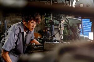 Engineer worker in production plant drilling at machine. Professional worker near drilling machine on factory. man inspecting and repairing machine for operation in workshop. photo