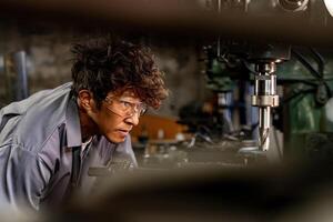 ingeniero trabajador en producción planta perforación a máquina. profesional trabajador cerca perforación máquina en fábrica. hombre inspeccionando y reparando máquina para operación en taller. foto