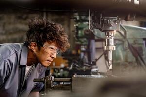 Engineer worker in production plant drilling at machine. Professional worker near drilling machine on factory. man inspecting and repairing machine for operation in workshop. photo