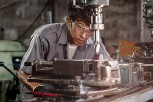 Engineer worker in production plant drilling at machine. Professional worker near drilling machine on factory. man inspecting and repairing machine for operation in workshop. photo