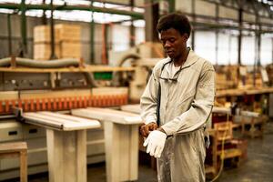 African man workers engineering standing with confidence with working suite dress and hand glove in front machine. Concept of smart industry worker operating. Wood factory produce wood palate. photo