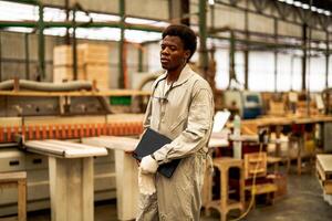 africano hombre trabajadores Ingenieria en pie con confianza con trabajando suite vestir y mano guante en frente máquina. concepto de inteligente industria trabajador operando. madera fábrica Produce madera paladar. foto