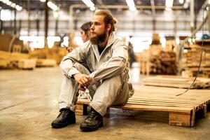 man workers engineering sitting with confidence with working suite dress and hand glove in front machine. Concept of smart industry worker operating. Wood factory produce wood palate. photo