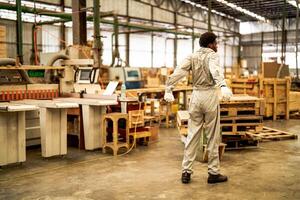 africano hombre trabajadores Ingenieria en pie con confianza con trabajando suite vestir y mano guante en frente máquina. concepto de inteligente industria trabajador operando. madera fábrica Produce madera paladar. foto