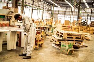 africano hombre trabajadores Ingenieria en pie con confianza con trabajando suite vestir y mano guante en frente máquina. concepto de inteligente industria trabajador operando. madera fábrica Produce madera paladar. foto
