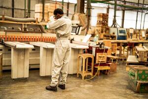 africano hombre trabajadores Ingenieria en pie con confianza con trabajando suite vestir y mano guante en frente máquina. concepto de inteligente industria trabajador operando. madera fábrica Produce madera paladar. foto