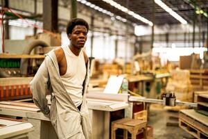 africano hombre trabajadores Ingenieria en pie con confianza con trabajando suite vestir y mano guante en frente máquina. concepto de inteligente industria trabajador operando. madera fábrica Produce madera paladar. foto