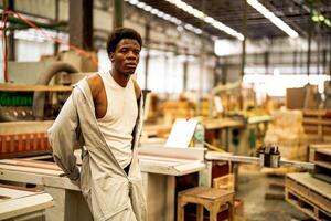 African man workers engineering standing with confidence with working suite dress and hand glove in front machine. Concept of smart industry worker operating. Wood factory produce wood palate. photo