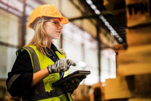 woman worker carpenter wearing safety uniform and hard hat working and checking the quality of wooden products at workshop manufacturing. man and woman workers wood in dark warehouse industry. photo