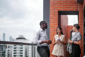 equipo de negocio personas inteligente hombre y mujer estar a al aire libre terraza edificio y hablar juntos con desayuno comida y café en el mano en bueno sensación con ciudad espacio edificio. negocio Mañana. foto