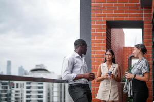 equipo de negocio personas inteligente hombre y mujer estar a al aire libre terraza edificio y hablar juntos con desayuno comida y café en el mano en bueno sensación con ciudad espacio edificio. negocio Mañana. foto