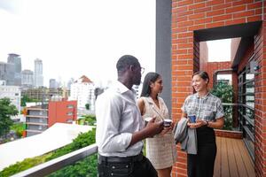 equipo de negocio personas inteligente hombre y mujer estar a al aire libre terraza edificio y hablar juntos con desayuno comida y café en el mano en bueno sensación con ciudad espacio edificio. negocio Mañana. foto