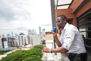 African business smart man stands at outdoor terrace building. people with on hand in good feeling with city space building. relaxing of people business morning. photo