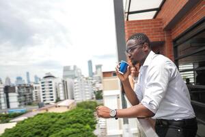 African business smart man stands at outdoor terrace building. people with on hand in good feeling with city space building. relaxing of people business morning. photo