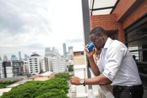 African business smart man stands at outdoor terrace building. people with on hand in good feeling with city space building. relaxing of people business morning. photo