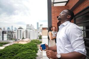 African business smart man stands at outdoor terrace building. people with on hand in good feeling with city space building. relaxing of people business morning. photo