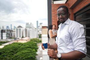 African business smart man stands at outdoor terrace building. people with on hand in good feeling with city space building. relaxing of people business morning. photo