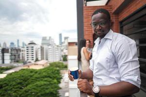 African business smart man stands at outdoor terrace building. people with on hand in good feeling with city space building. relaxing of people business morning. photo