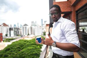 African business smart man stands at outdoor terrace building. people with on hand in good feeling with city space building. relaxing of people business morning. photo