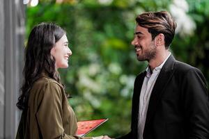 Businessman and casual businesswoman shaking hands outdoors. Two young multicultural coworkers deal for success. background of  green wall nature trees. photo