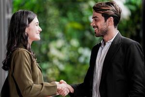 Businessman and casual businesswoman shaking hands outdoors. Two young multicultural coworkers deal for success. background of  green wall nature trees. photo