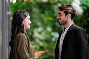 Businessman and casual businesswoman shaking hands outdoors. Two young multicultural coworkers deal for success. background of  green wall nature trees. photo