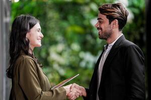 Businessman and casual businesswoman shaking hands outdoors. Two young multicultural coworkers deal for success. background of  green wall nature trees. photo