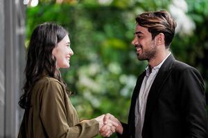 Businessman and casual businesswoman shaking hands outdoors. Two young multicultural coworkers deal for success. background of  green wall nature trees. photo