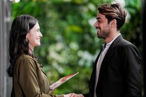 empresario y casual mujer de negocios sacudida manos al aire libre. dos joven multicultural compañeros de trabajo acuerdo para éxito. antecedentes de verde pared naturaleza arboles foto