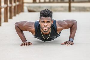 Motivated black sportsman doing push ups in park photo