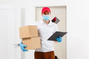 un hombre un médico máscara y azul caucho guantes con un caja, un paquete o empaquetar en su manos. comida entrega durante el cuarentena de el coronavirus pandemia. hogar entrega, en línea orden. en línea compras . foto