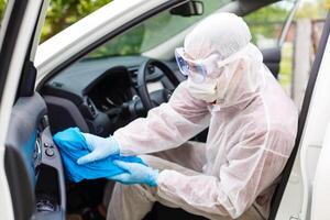 desinfectante trabajador personaje en protector máscara y traje aerosoles bacteriano o virus en un coche. foto