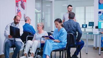 Doctor with stethoscope holding disabled senior woman radiography in wheelchair while talking with her in hospital waiting area. Patient asking about his appointment at clinic reception. photo