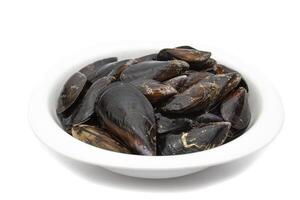 Raw mussels in a white bowl, isolated on white background. It feeds on phytoplankton and zooplankton, and even decomposing organic particles found in seawater, by filtering it through its gills. photo