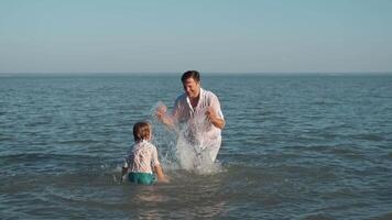 vader en zoon verstuiven elk andere met water terwijl zwemmen in de oceaan. video