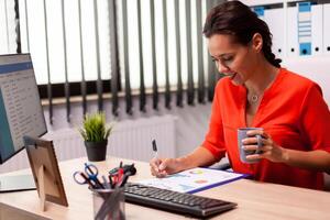 profesional mujer de negocios empresario leyendo Finanzas análisis mirando a corporativo cartas vistiendo rojo. exitoso financiero auditor en datos marketing mirando a gráficos en computadora pantalla y escritura informe. foto