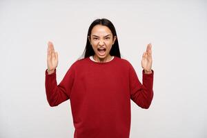 Young lady, angry asian woman with dark long hair. Wearing red sweater and shouting irritably at you with hands lifted. Enough, fed up with this. Watching at the camera isolated over white background photo