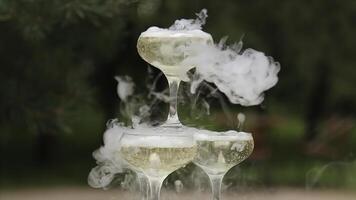 Glasses Of Champagne Smoking. Champagne glasses. Smoke Billowing Over A Champagne Flute. Catering service. Wedding slide champagne for bride and groom outdoors. Colorful glasses for alcohol. Business photo