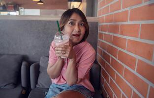 Woman sitting on sofa in the coffee shop holding smooth juice in plastic and drinking smooth healthy eating fruit with funny face,Enjoying lifestyle concepts,happines holiday. photo