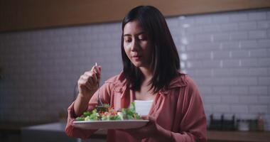 beeldmateriaal van jong Aziatisch vrouw aan het eten groente salade in keuken Bij thuis, gezond voedsel en welzijn concept video