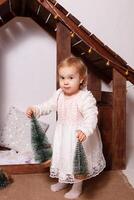 A little girl with toys in a wooden house. Photo studio with Christmas decorations. A happy child plays with toys, Artificial little Christmas trees.