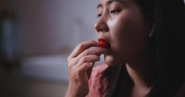 metraggio vicino su di giovane asiatico donna nel senza fili cuffie godendo degustazione pomodoro nel cucina a a casa, sano cibo e benessere concetto video