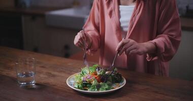 metraggio vicino su di giovane asiatico donna mescolare verdura insalata con un' forchetta nel cucina a a casa, sano cibo e benessere concetto video