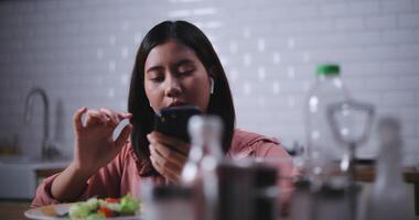 imágenes de joven asiático mujer sentado a un mesa disfrutando un ensalada y utilizar teléfono inteligente tomando un foto en cocina a hogar, saludable comida y bienestar concepto video